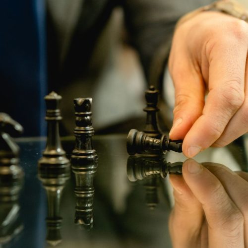 Hand moves chess piece in strategic game setting, reflecting planning and decision-making.